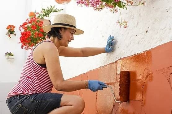 A woman repainting an exterior wall of a house