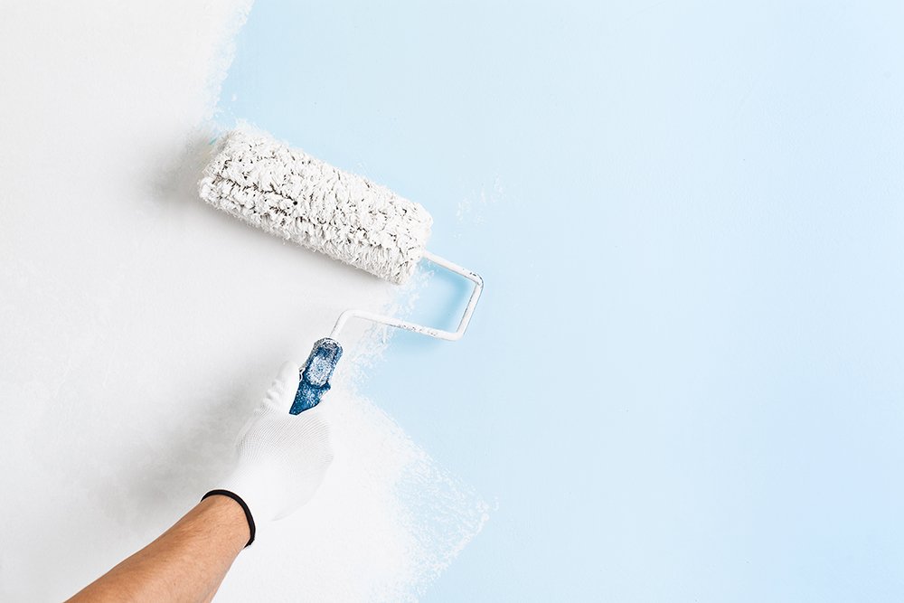 A professional uses a roller to spread light blue paint onto drywall