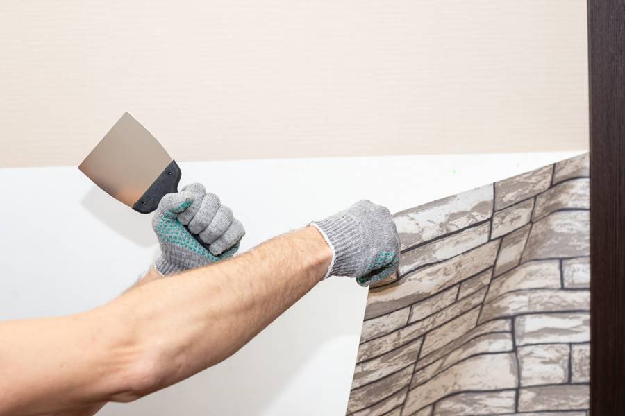 A professional removes brick-patterned wallpaper from a wall