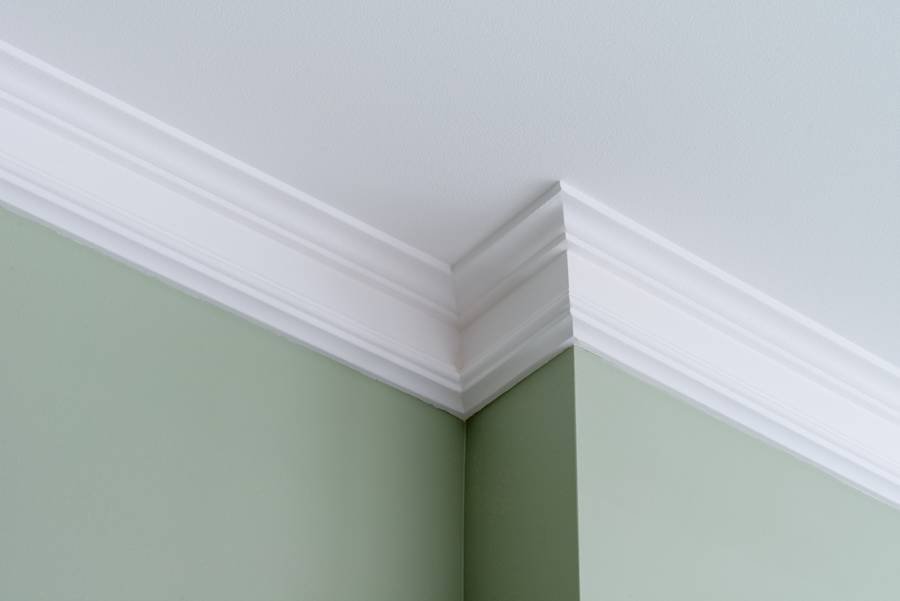 Decorative white crown molding between a green wall and white ceiling