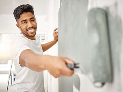 A smiling professional painter rolls gray paint onto a wall