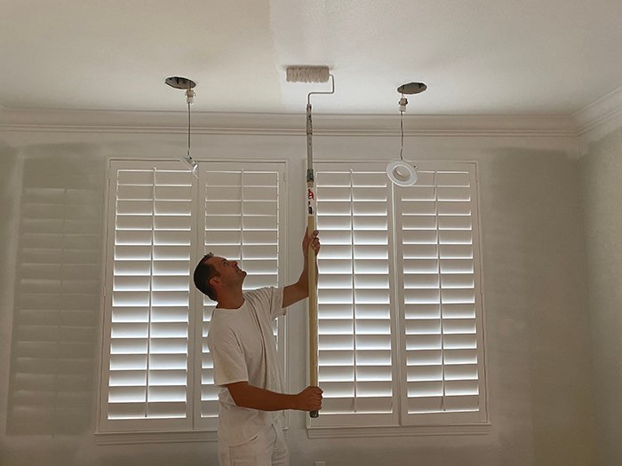 A professional uses a roller to paint a home’s ceiling