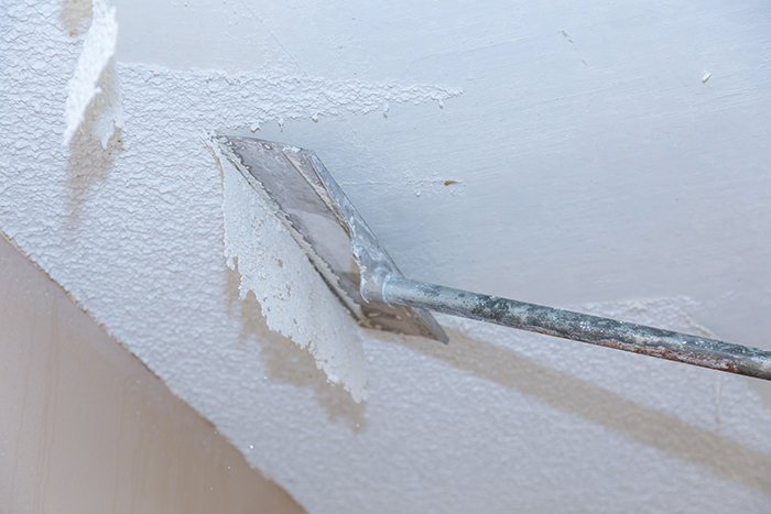 A professional scrapes texture off a ceiling