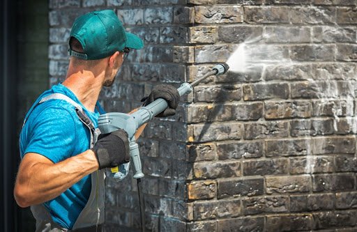 A professional power washes a brick home’s exterior in preparation for painting