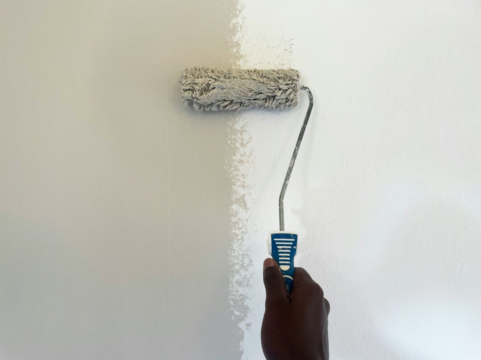 A white wall being painted gray using a short paint roller