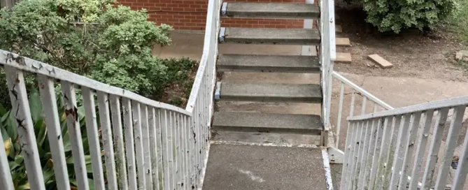 Metal railings with cracked white paint accompanying concrete outdoor stairs