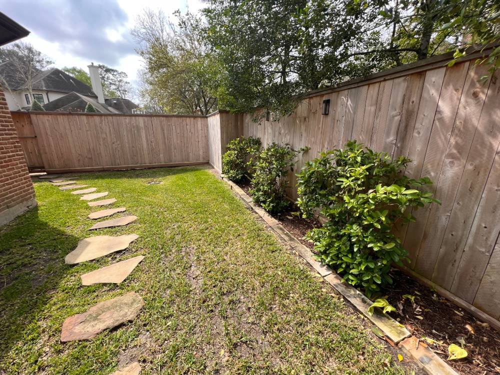 A tall, recently stained wooden fence surrounds a yard and stone path