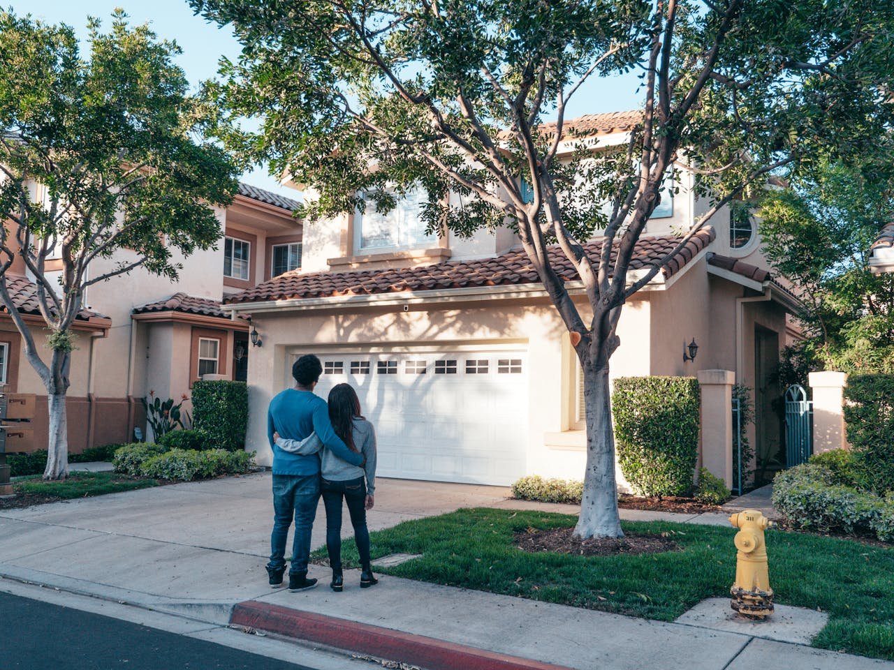Couple standing arm in arm on the driveway, looking at their freshly painted suburban home