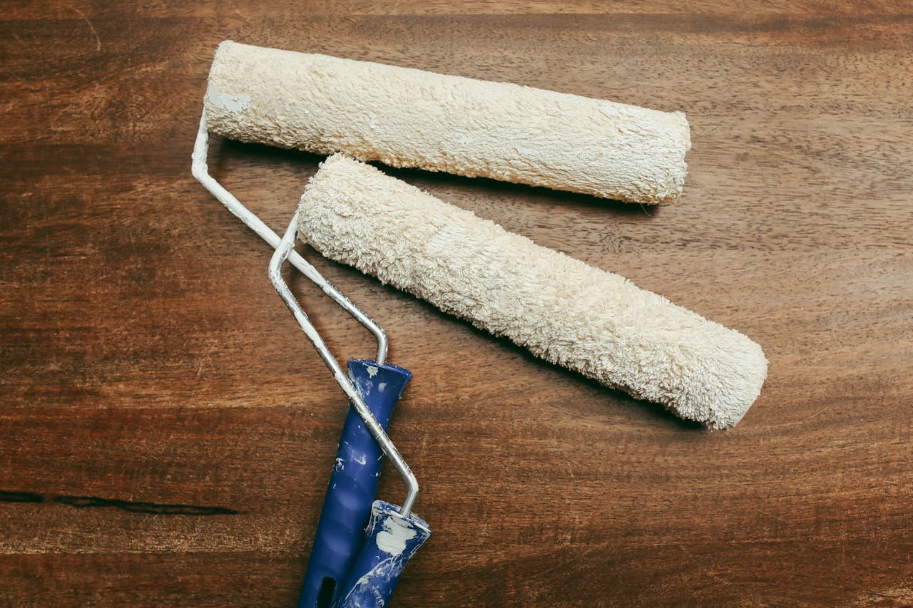 Two used paint rollers with blue handles resting on a wooden surface