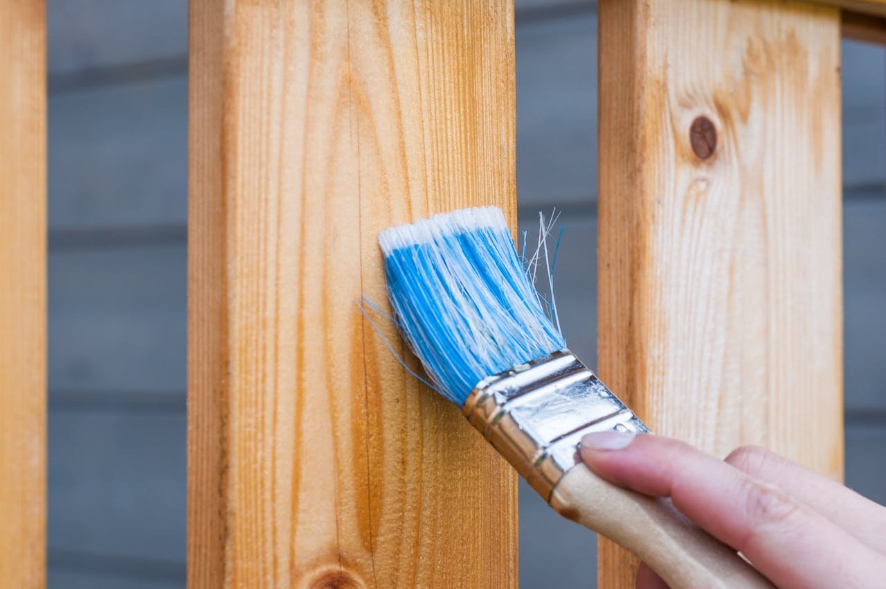 Close-up of a hand applying a fresh coat of paint to an exterior wood railing